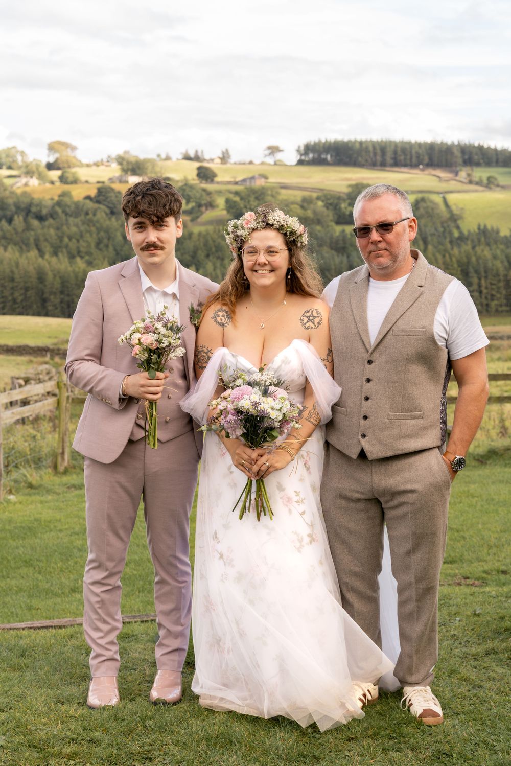 Wedding party poses outdoors in rustic country setting wearing beige and brown attire with floral bouquets.