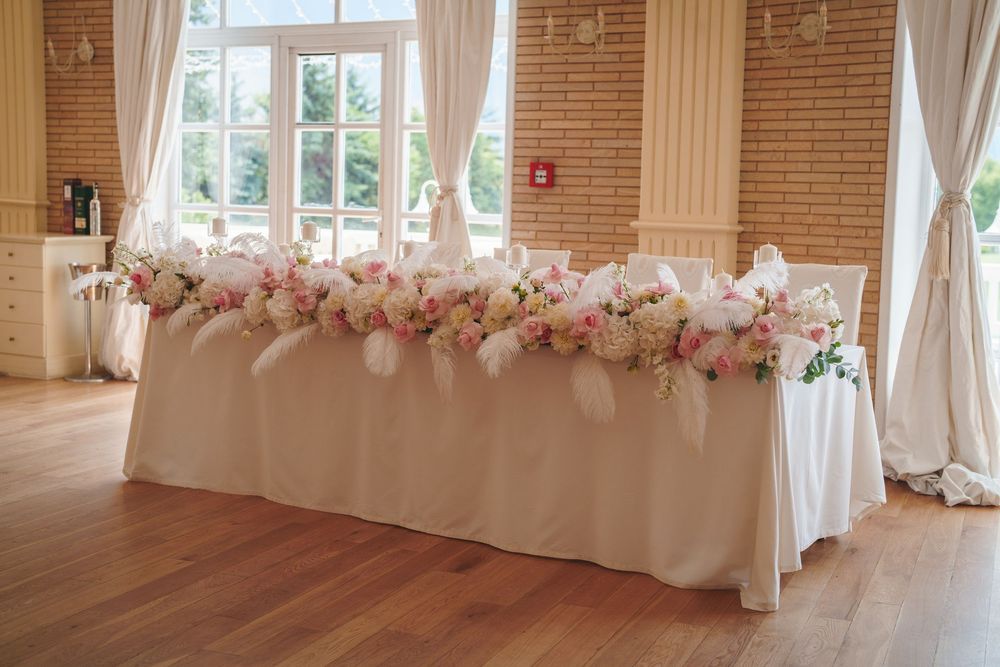 An elegant wedding reception venue with exposed brick walls, white drapes, and pink floral arrangements along the tables.