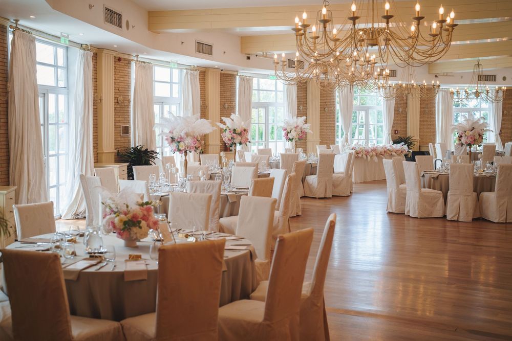 Elegant wedding reception hall with hardwood floors, crystal chandeliers, and white-draped tables set for a formal event.