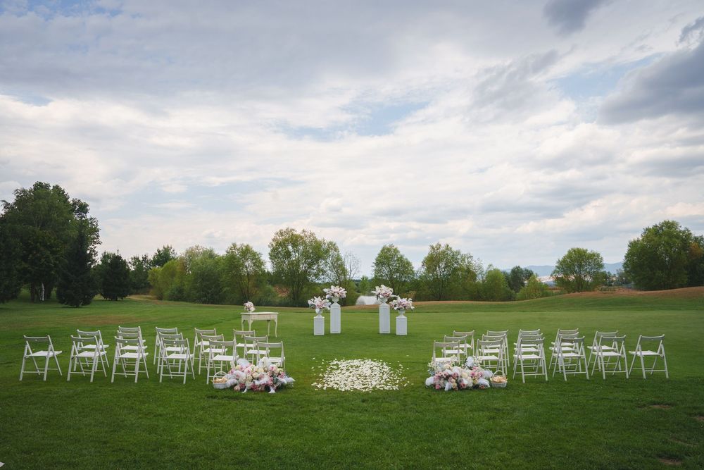 White folding chairs arranged in a semi-circle on a lush green lawn for an outdoor wedding ceremony under cloudy skies.