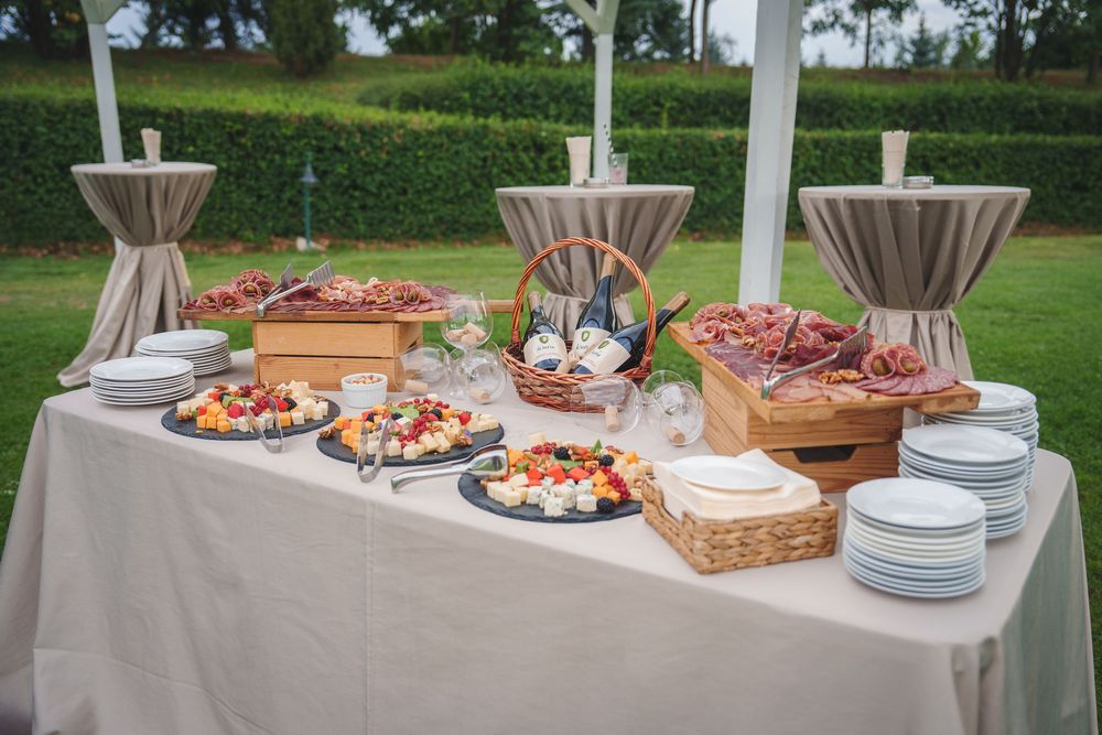 Elegant buffet table with appetizers, plates and decorative baskets displayed on white linens at an outdoor event.