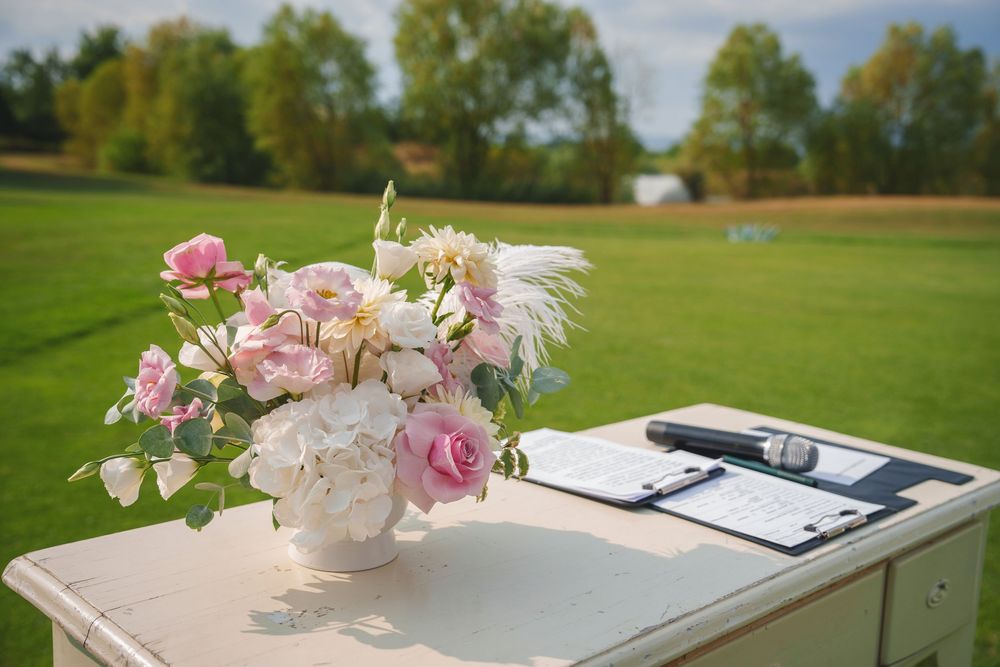 A collection of pink floral arrangements and clipboards displayed on white tables at an outdoor event venue.