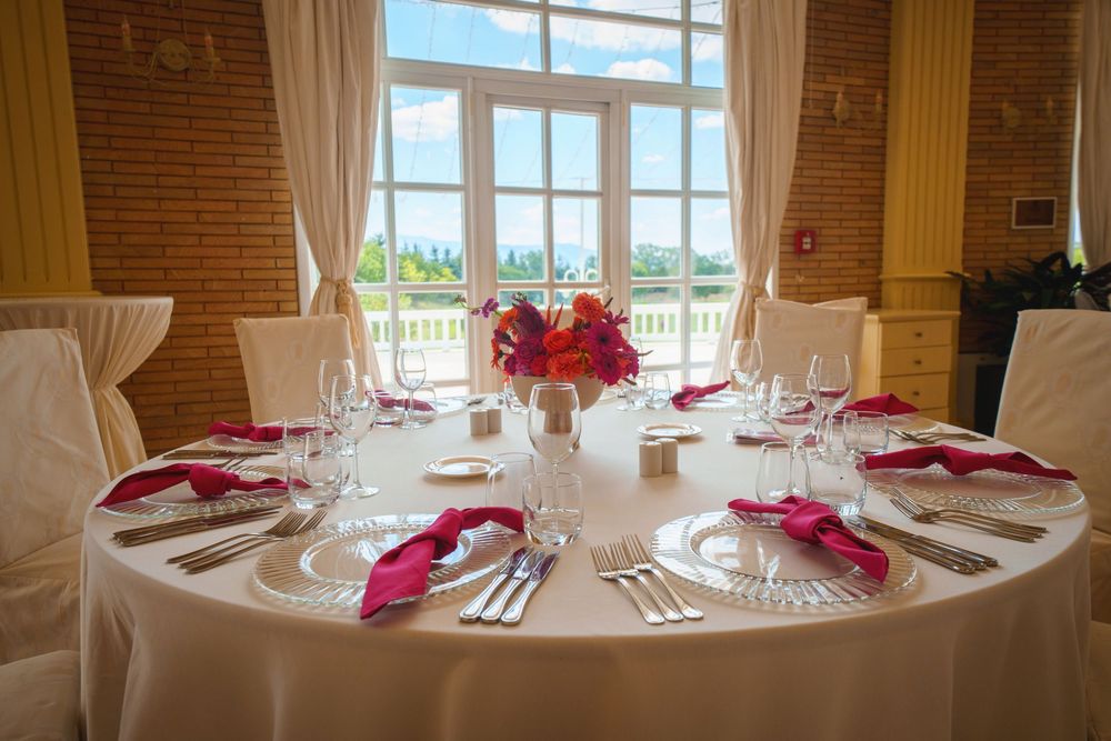 Elegant dining room with large windows, white tablecloths, and vibrant pink floral centerpieces in a brick-walled venue.