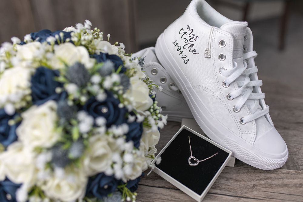 White baby shoes and delicate floral bouquet with white and blue flowers arranged on wooden surface.