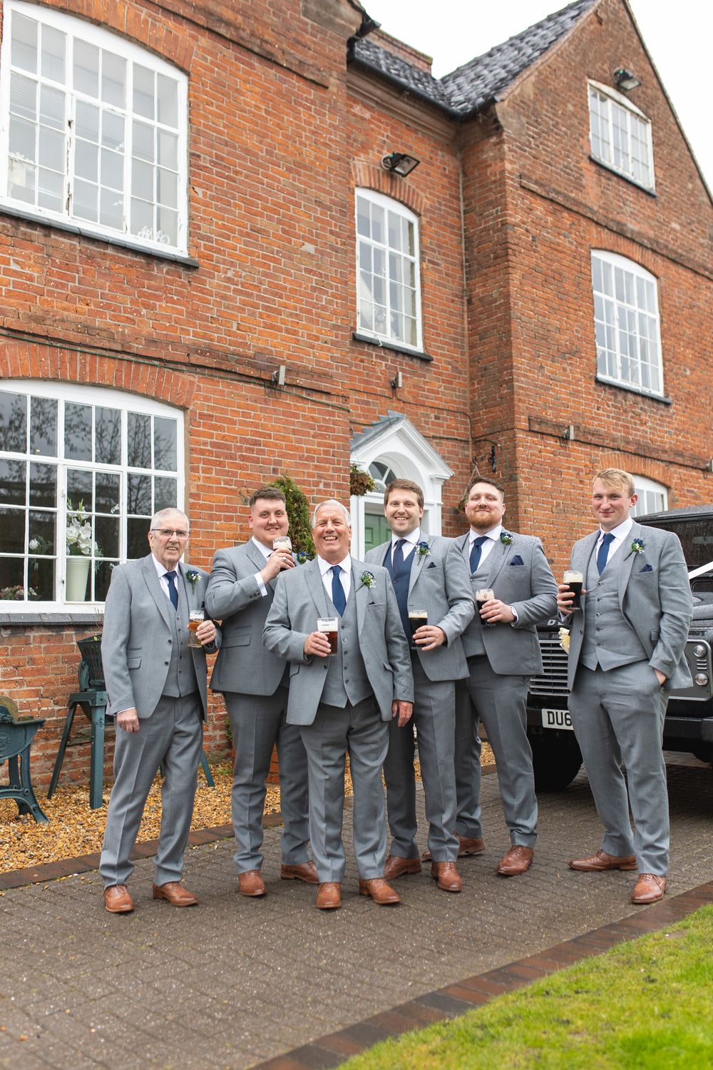 A wedding party in matching grey suits poses for a photo outside a classic red brick building.