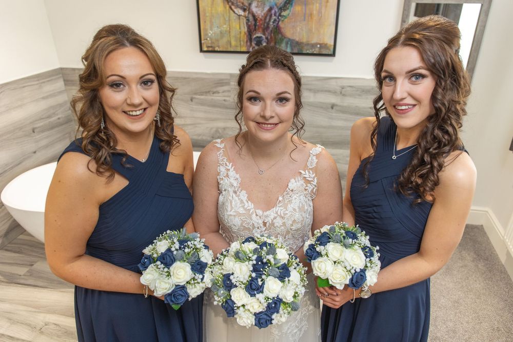 A group in navy blue and white formal attire pose together holding blue and white floral bouquets.