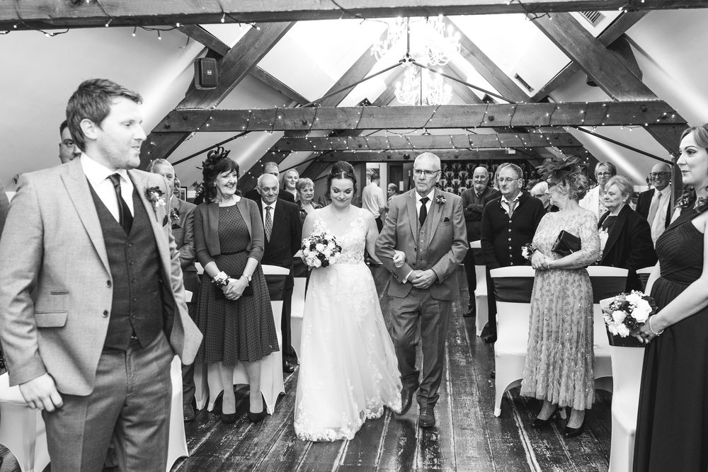 A wedding celebration takes place in a rustic venue with exposed wooden beams and gathered guests.