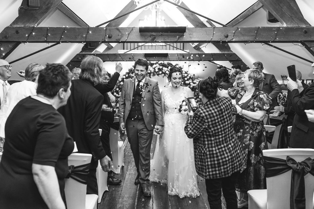 Black and white photo of wedding guests mingling under tent structure at reception.