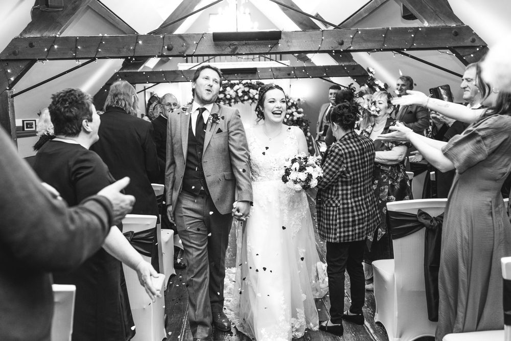 Monochrome image of wedding celebration with guests gathered under decorated tent canopy.