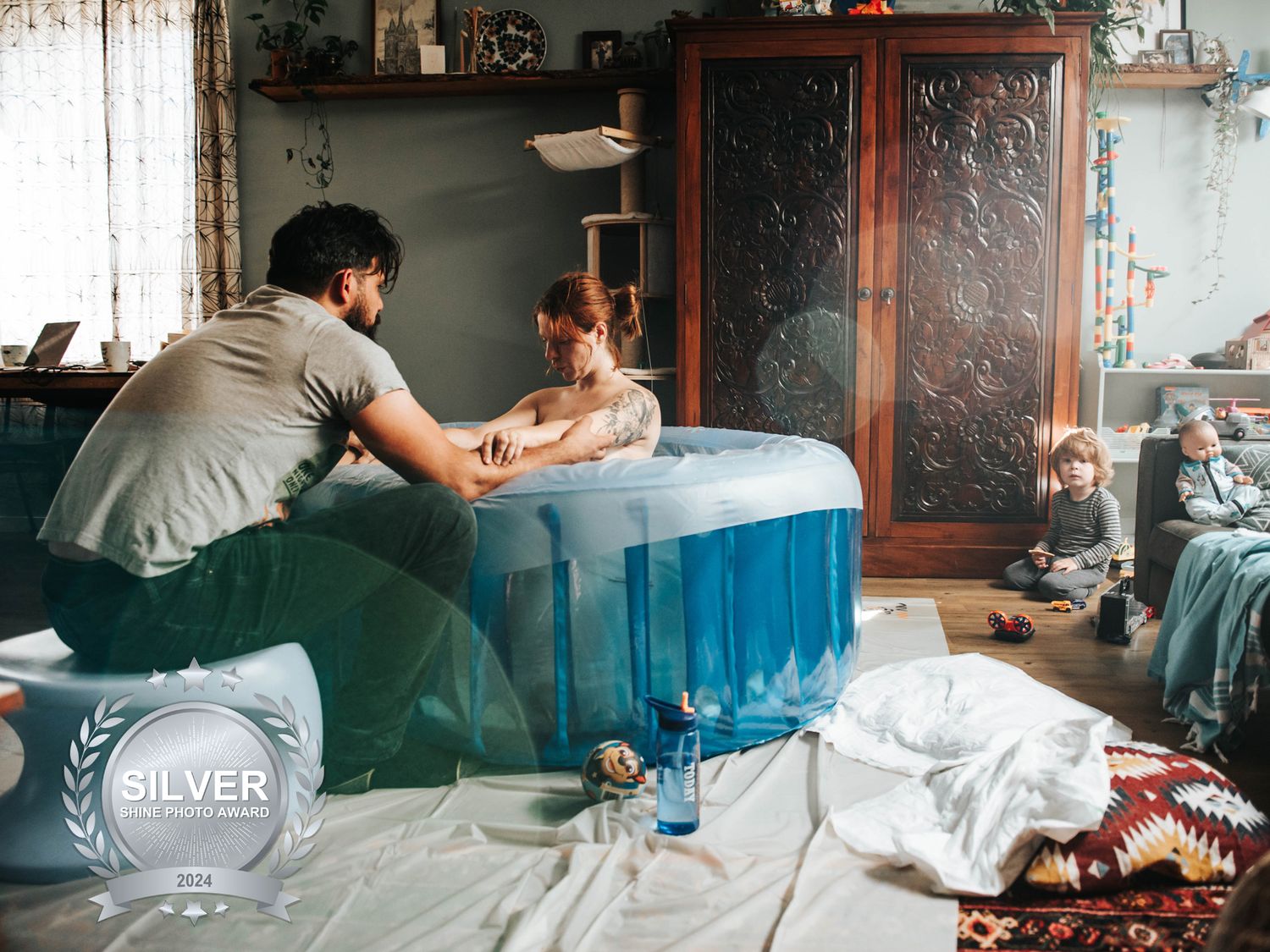 Silver Shine Photo Award winning birth photo of a father supporting a woman in a birthing pool.