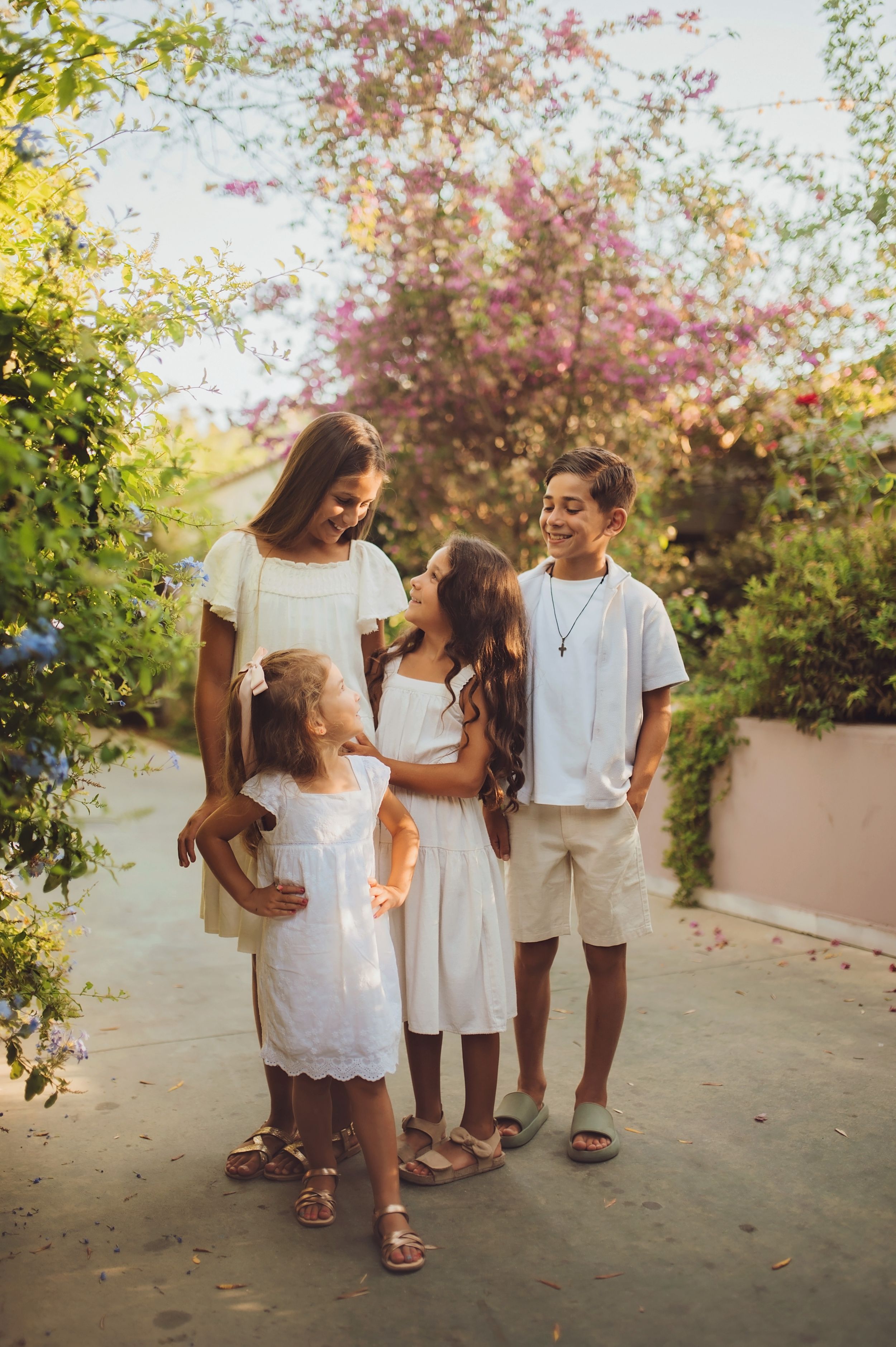 A family shares a joyful moment together on a garden path surrounded by blooming trees at sunset.