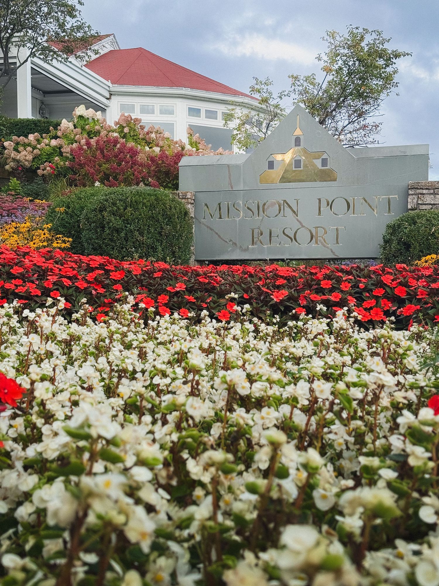 A field of vibrant white and red flowers blooms in front of the Mission Point Resort entrance sign.