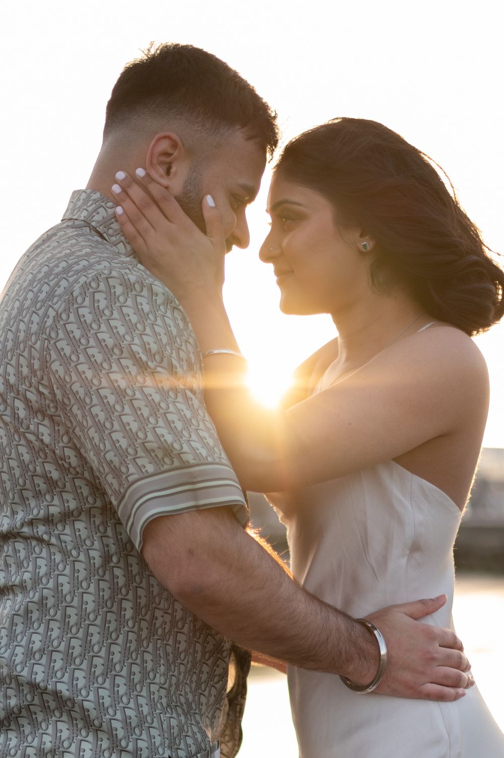 Couple sharing intimate almost-kiss moment backlit by stunning golden sunset during beach engagement session.