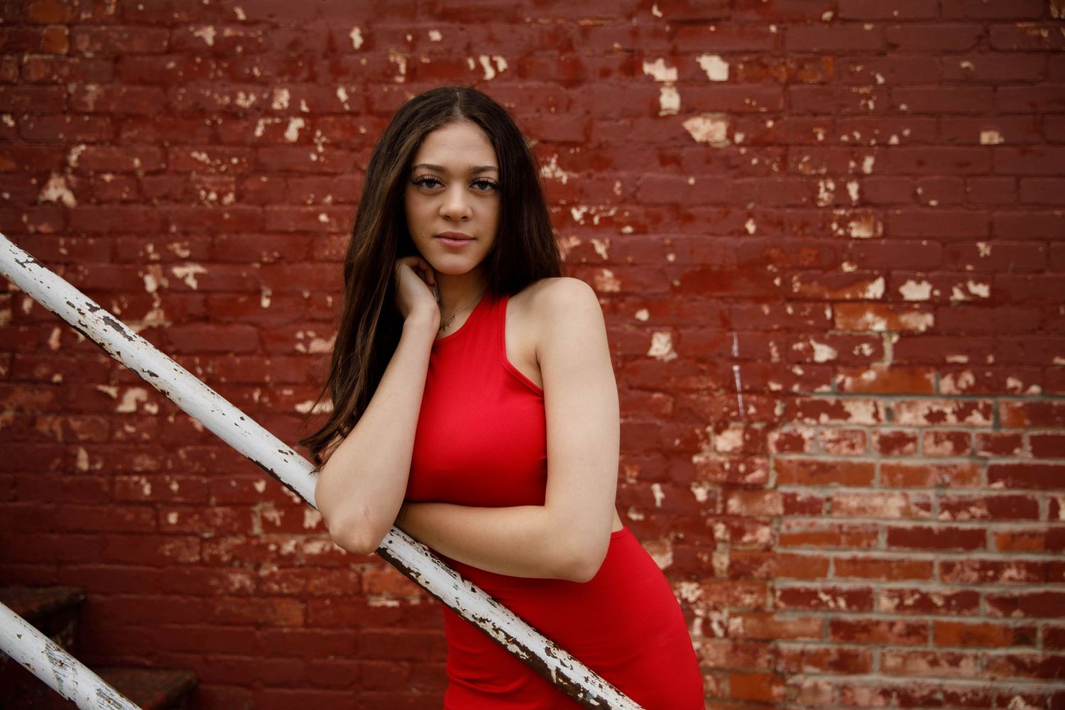 A person in a sleeveless red dress poses against a weathered brick wall in a series of casual shots.