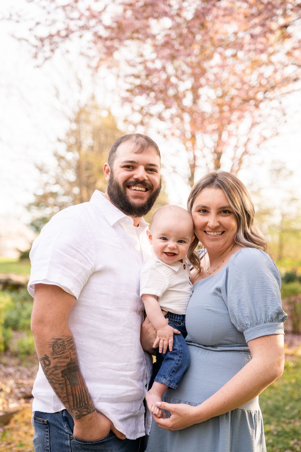 A family poses together outdoors during autumn with pink cherry blossoms in the background.