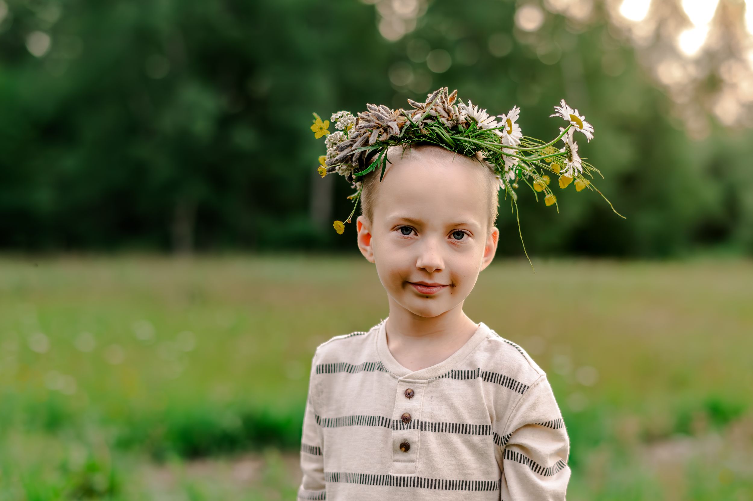 A child wearing a delicate floral crown sits in a lush green field during golden hour.