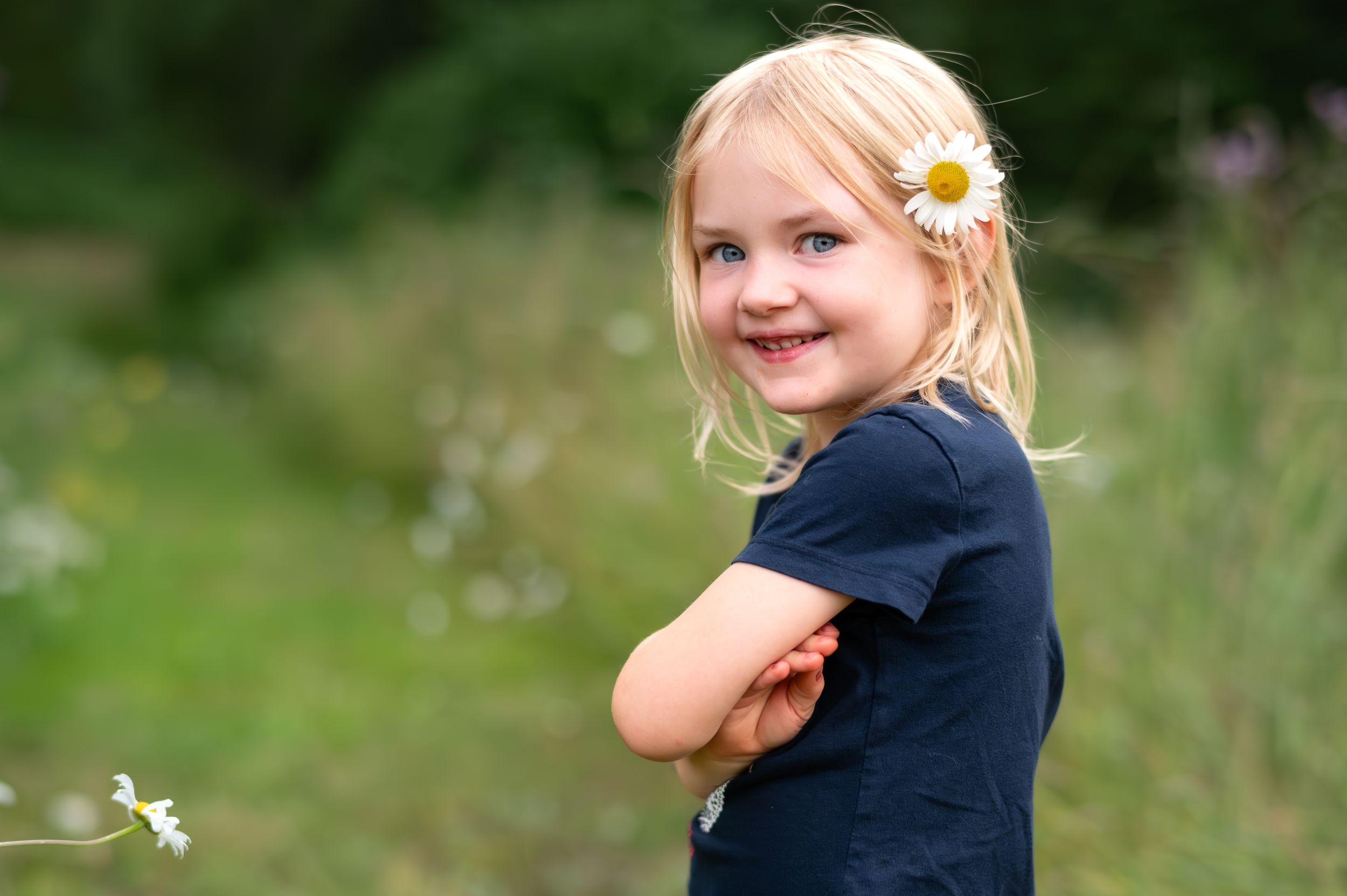A young girl in a navy dress plays in a field of wildflowers on a sunny summer day.