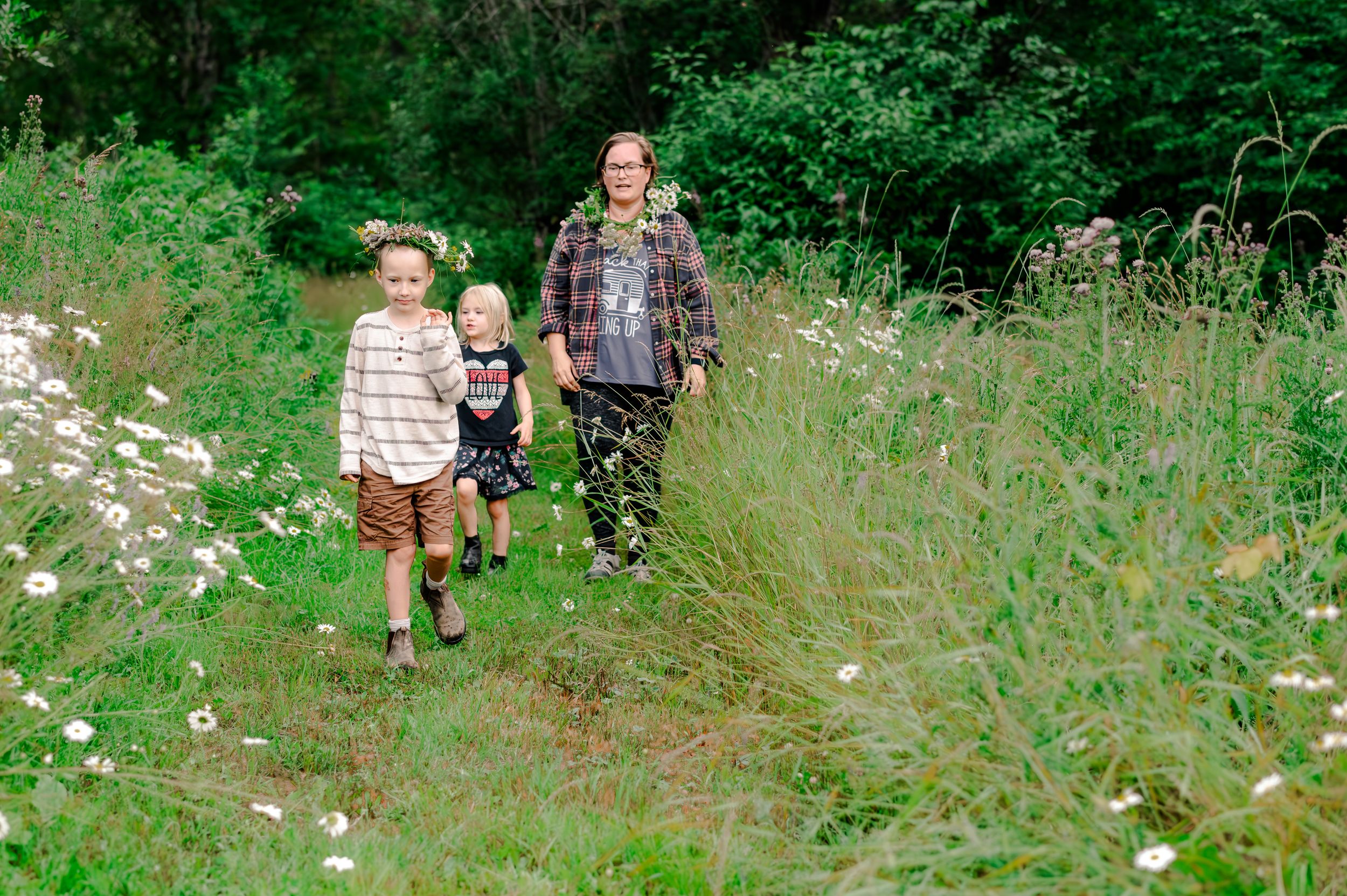 People walking along a lush green trail through tall grass and wildflowers in summer.