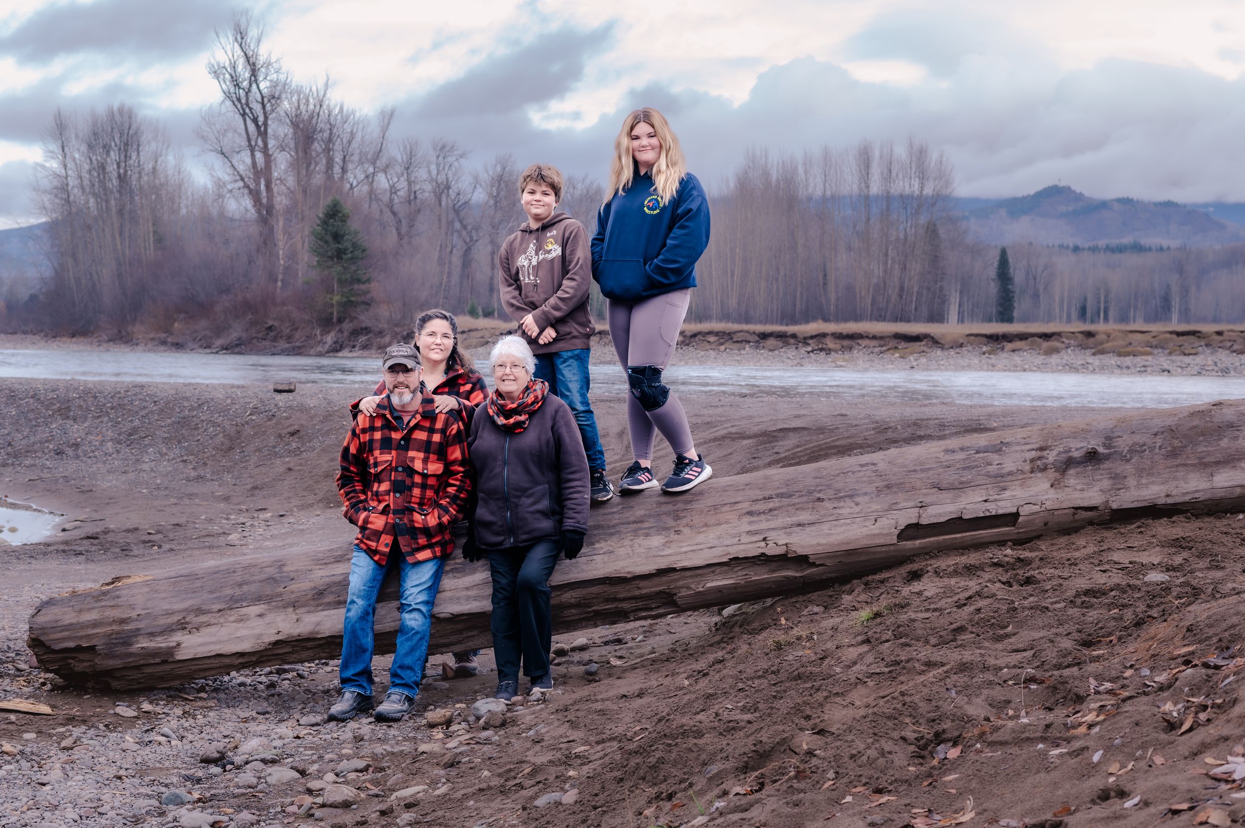 Family enjoying a winter day together on a muddy riverbank with mountains in the background.
