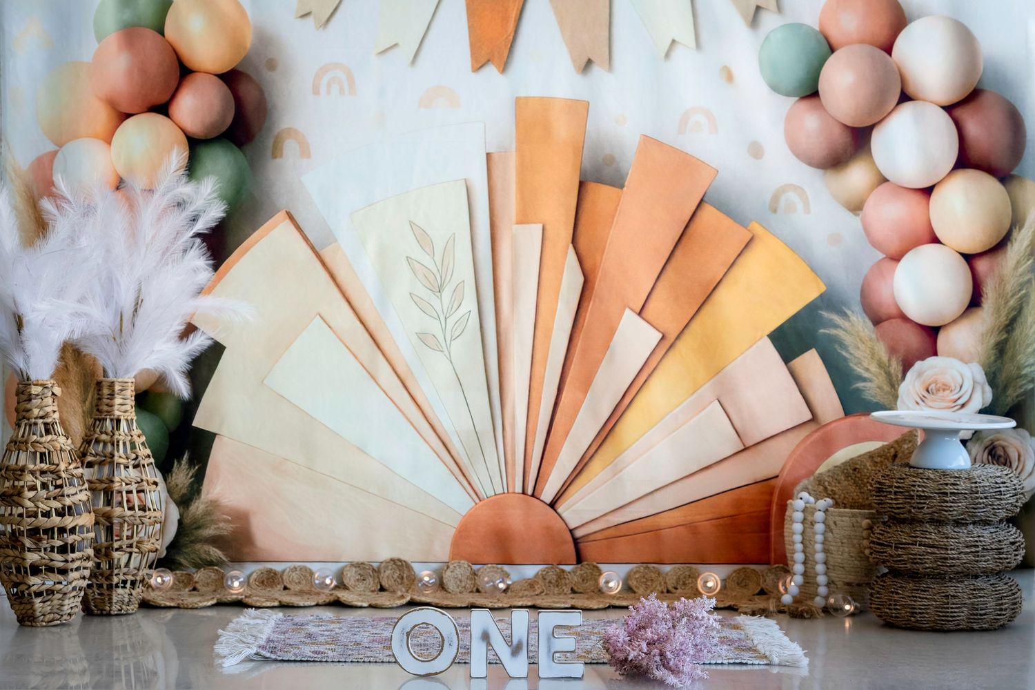 Pastel paper fan backdrop with 'ONE' text, balloon garland, and rustic decor for a first birthday party setup.