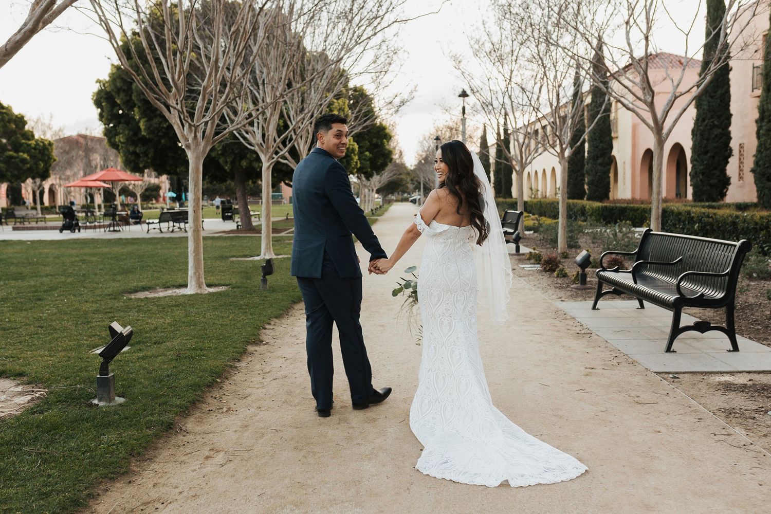 A couple shares a romantic moment on a tree-lined path during their wedding photoshoot at sunset at Stone Brewing in San Diego.