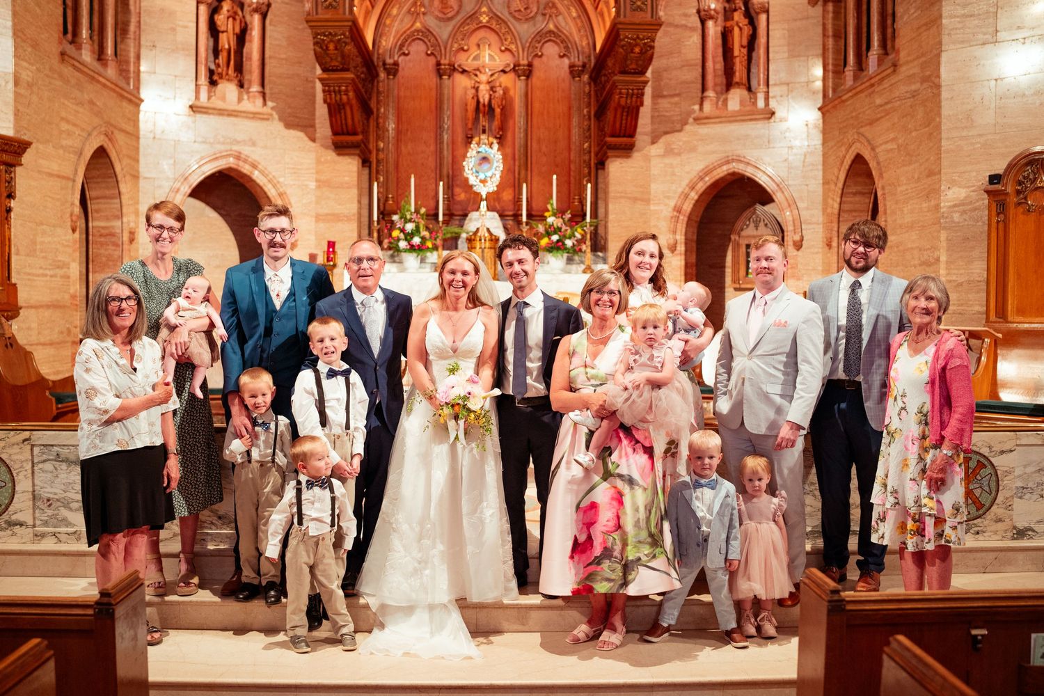 Wedding party poses for group photos inside ornate stone church with arched doorways and warm lighting.