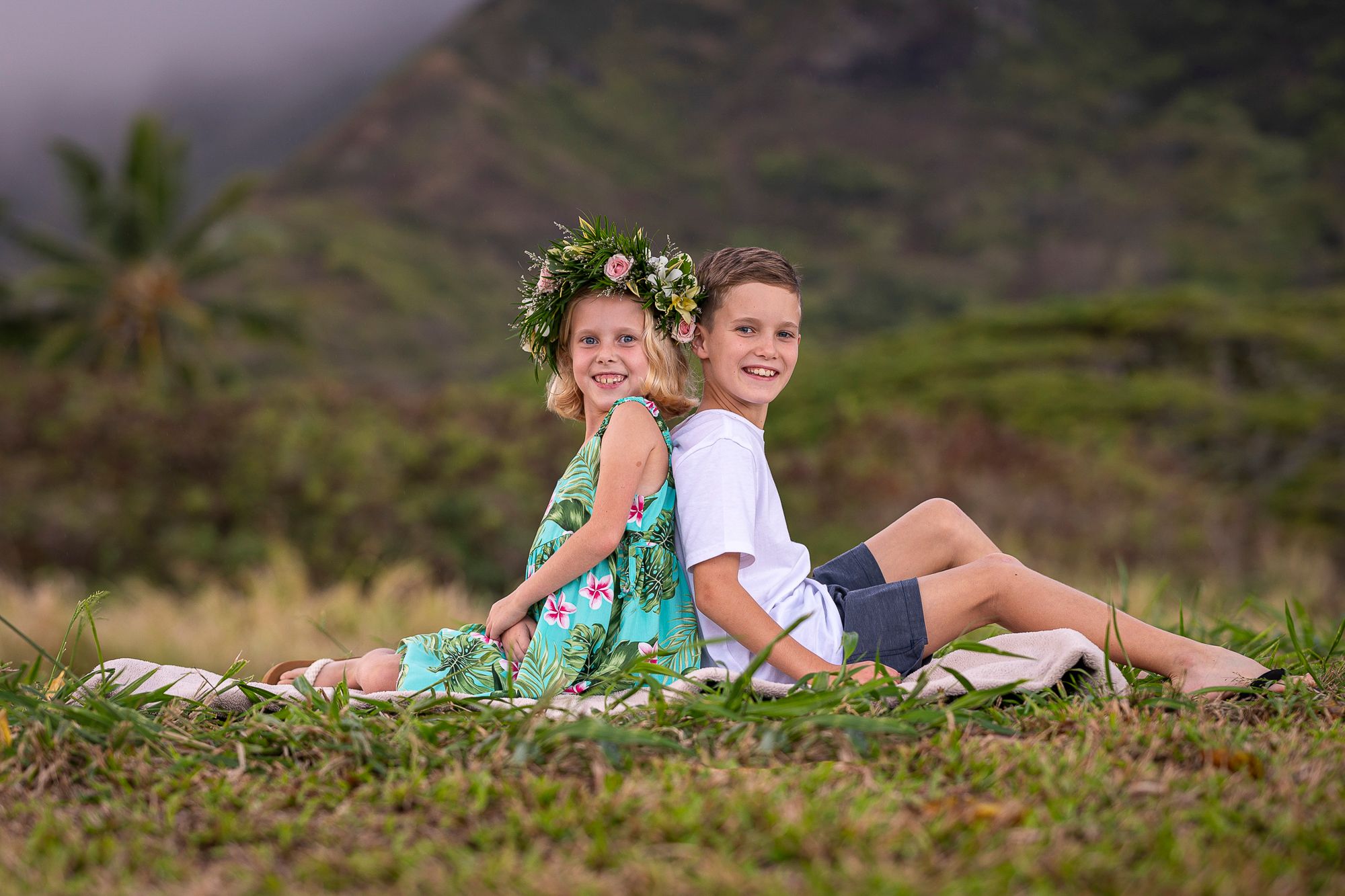 Brother and sister on grass at Kualoa Ranch for Oahu Family Photos with mountains in background during sunset.