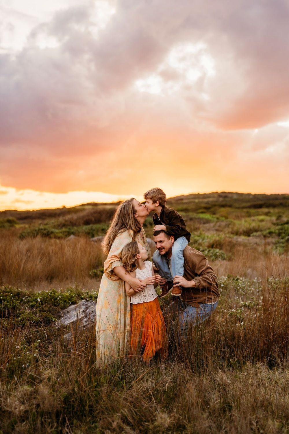 Family shares tender moments together in a golden field at sunset while wearing bohemian style clothing at their Sydney family photoshoot