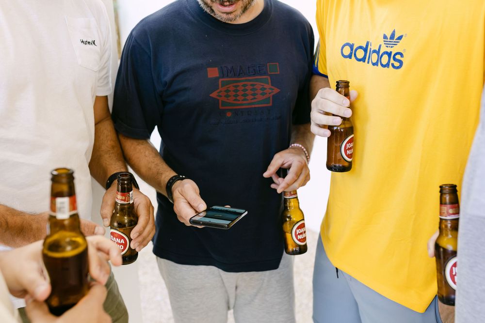 Groomsmen checking a phone while holding beers during relaxed wedding morning in Cascais.