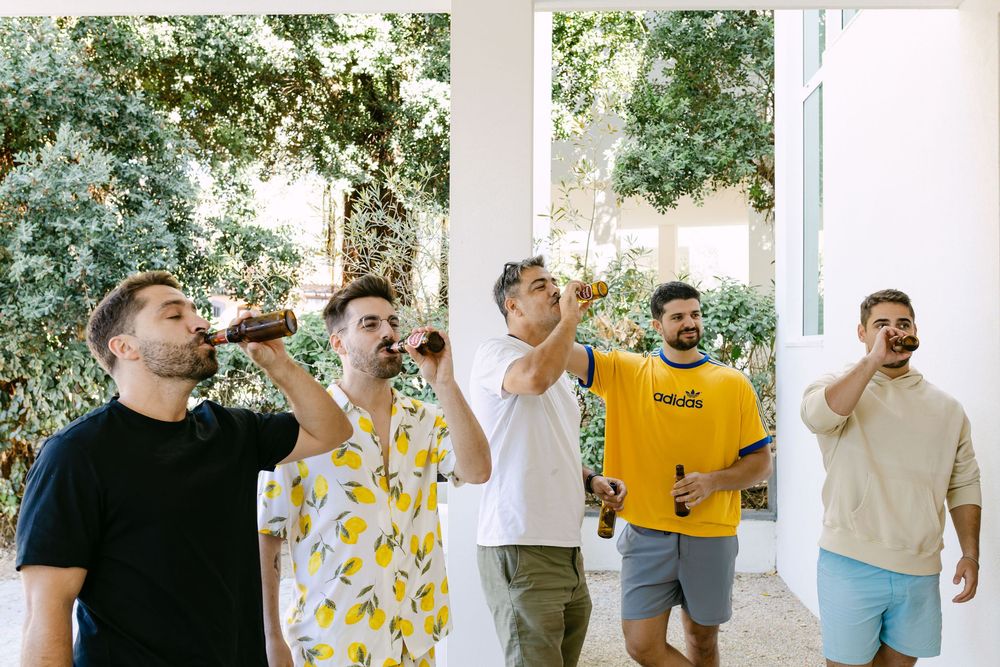 Groom and friends toasting beers on balcony before wedding ceremony near the sea in Lisbon.