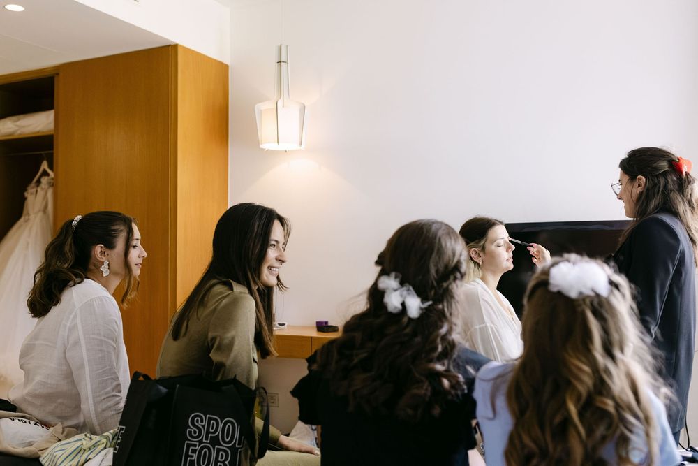 Bridesmaids watching bride’s makeup with smiles during intimate wedding morning in Cascais.