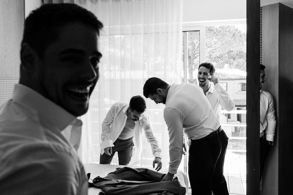 Black and white candid of groomsmen laughing while getting dressed in Cascais.