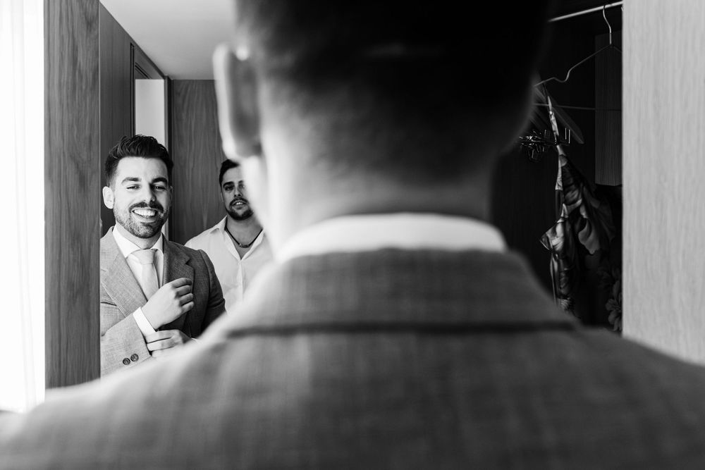 Groom adjusting his tie in front of the mirror during wedding preparations in Cascais, Lisbon.