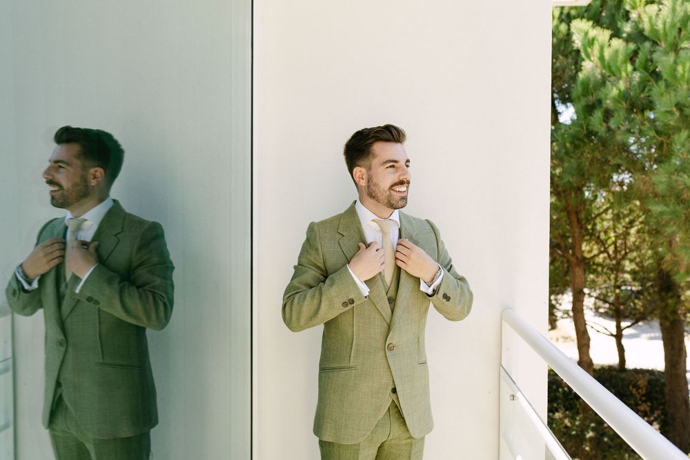 Groom adjusting his jacket on a sunlit balcony before wedding ceremony near the sea in Cascais.
