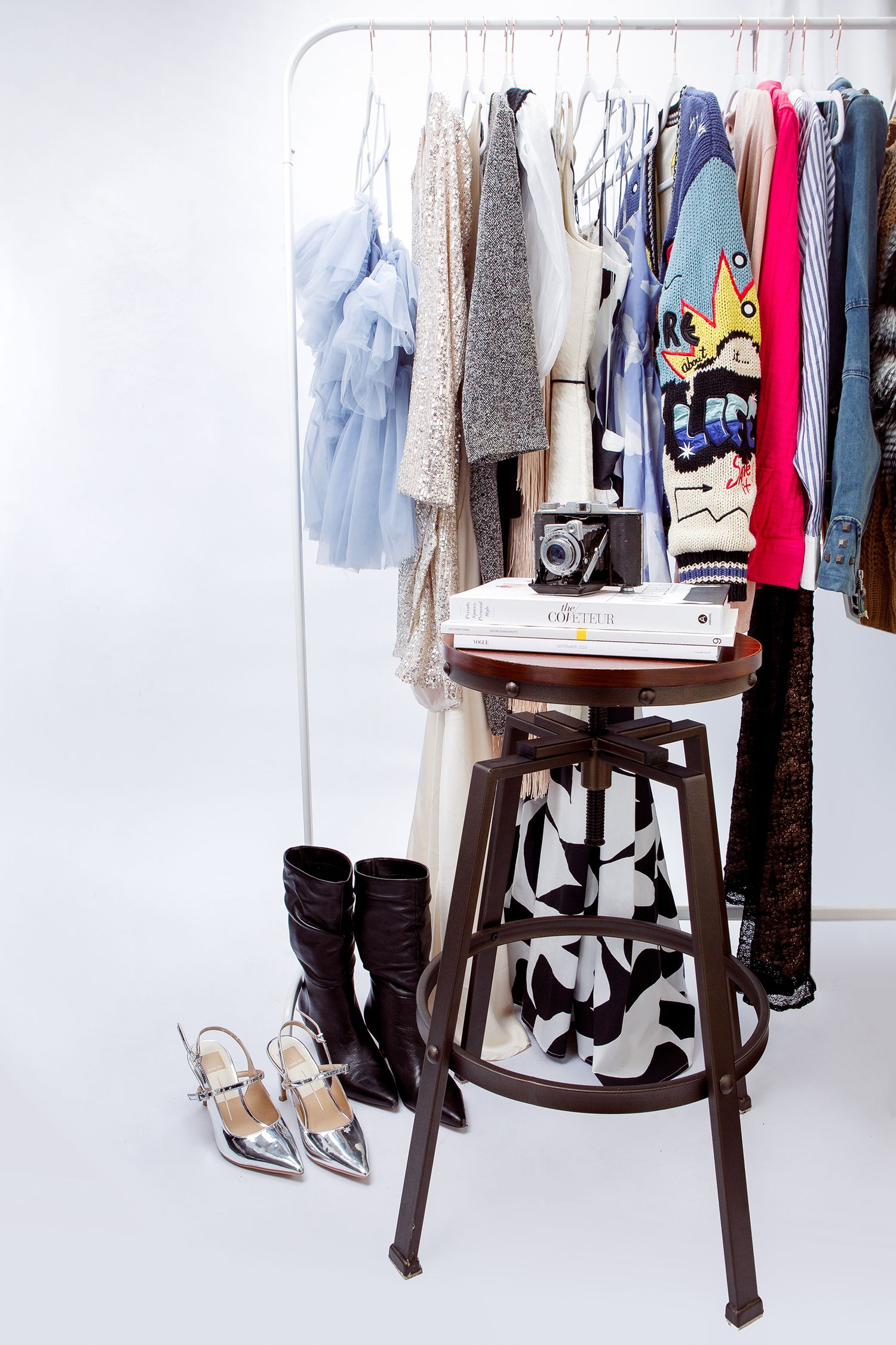 Stylish clothing display with boots and hangers on wooden stands showing fashion items against a white background.