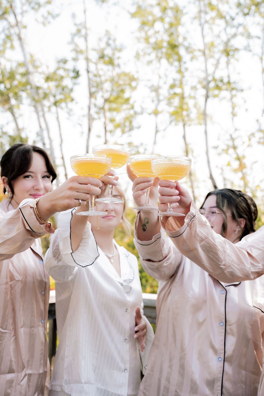 A group in light pink attire raises champagne glasses in a celebratory toast outdoors.