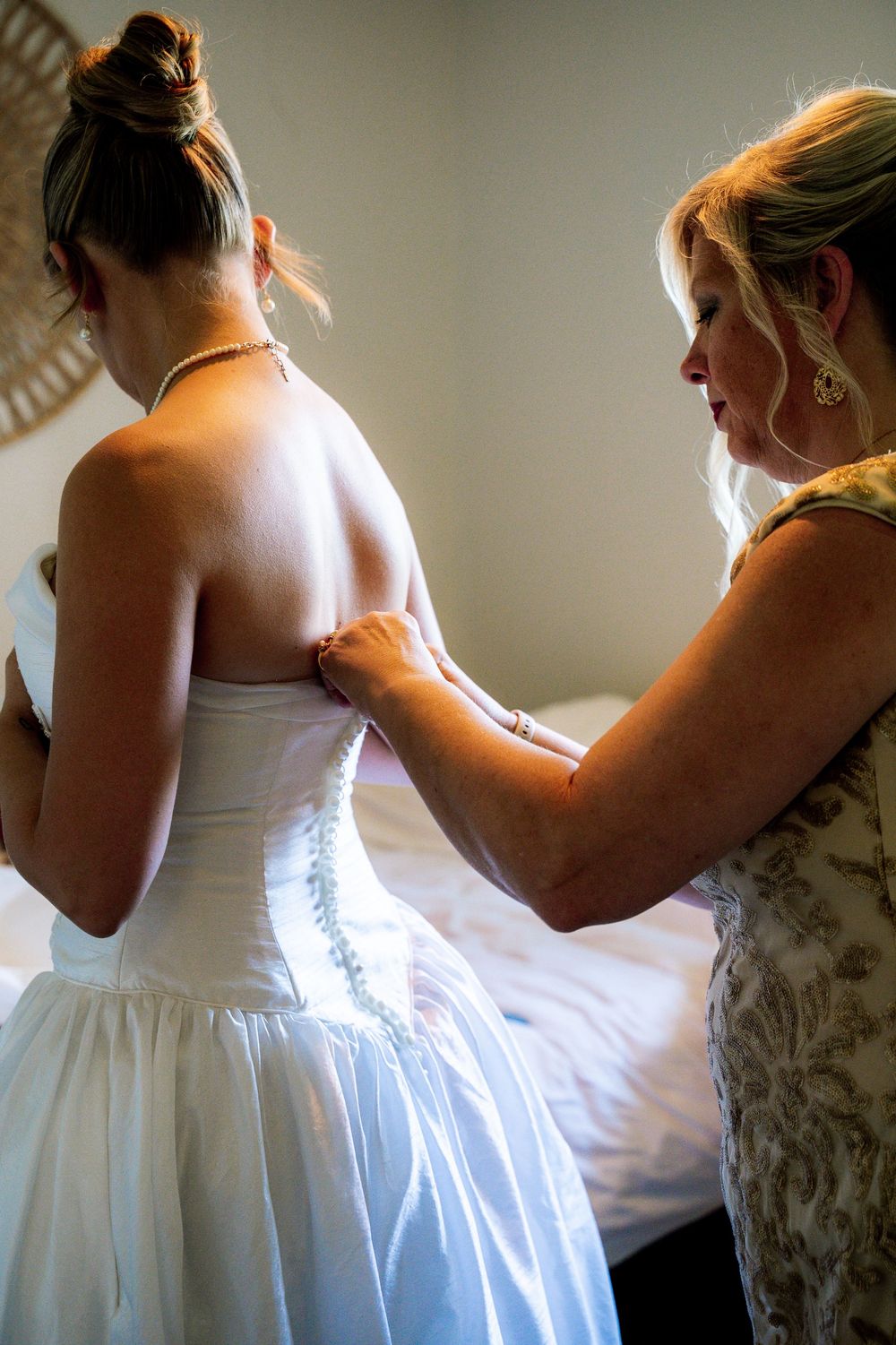 A series of photos showing a white wedding dress being laced up and adjusted in soft natural lighting.