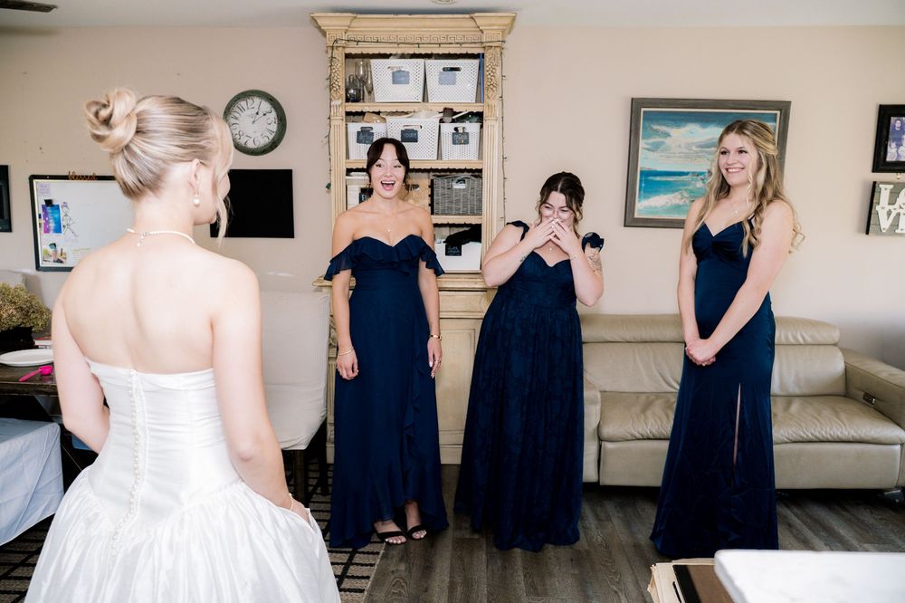 A wedding party group photo series showing people in navy blue dresses and a white gown in a room with framed artwork.