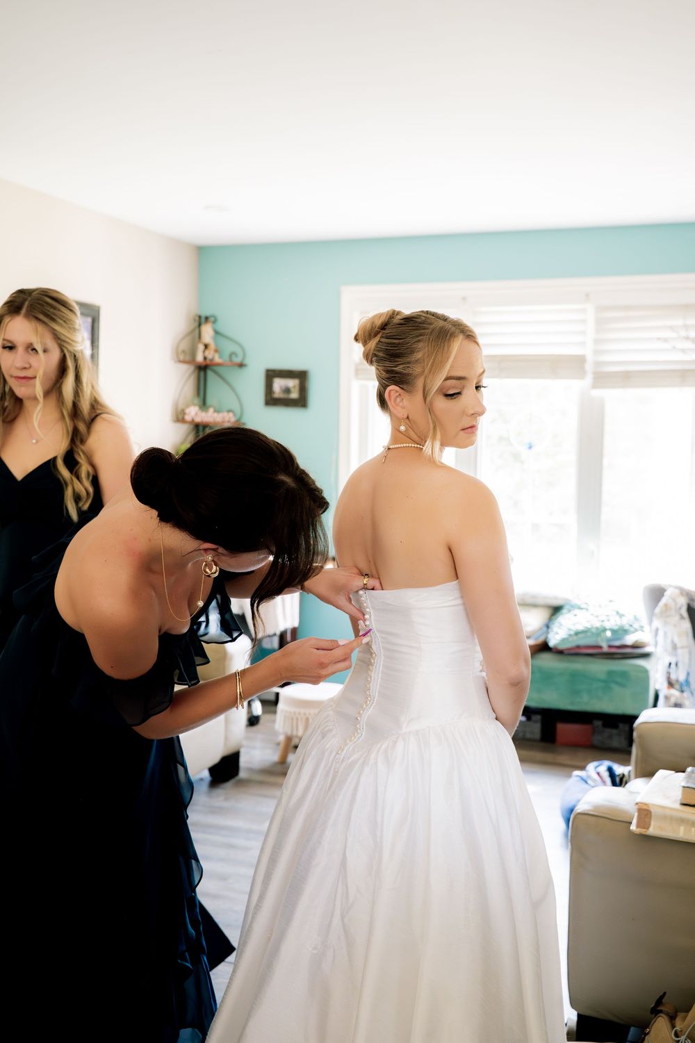 Someone helps with the lacing and final adjustments of a white wedding dress in a room with mint green walls.