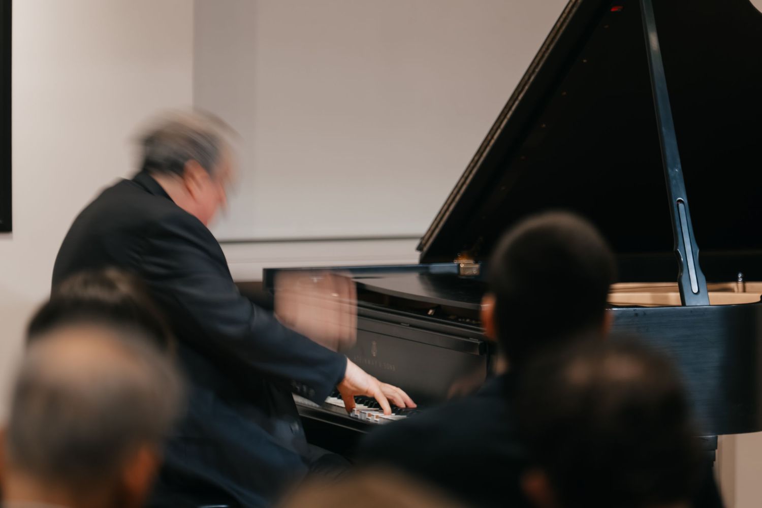 A pianist performs at a grand piano while an audience watches from their seats during a classical concert.