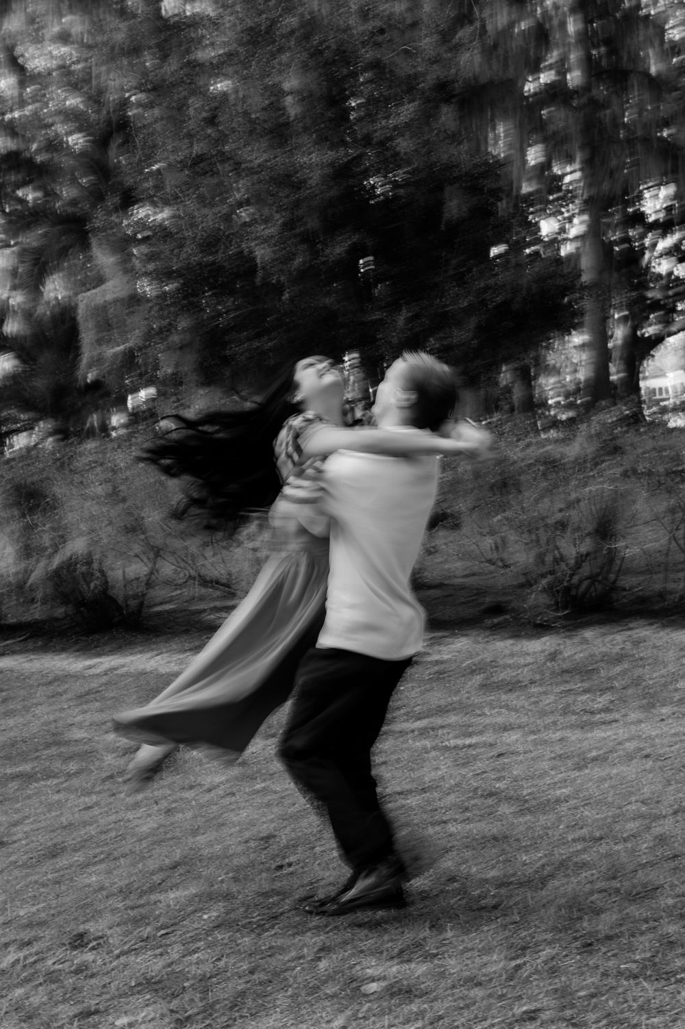 Black and white motion blur photo of two people dancing together in an outdoor setting.