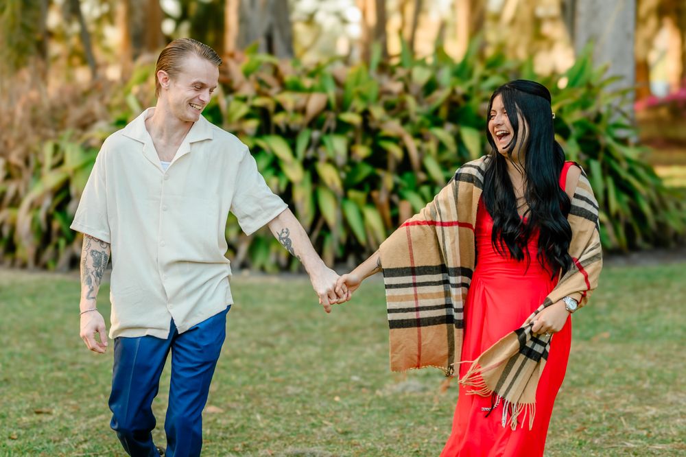 A couple walking together through a lush garden path with palm trees and greenery.