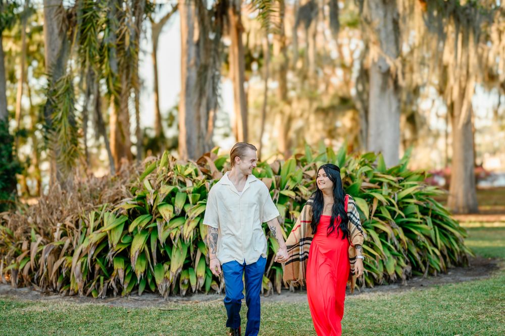 Two people strolling along a scenic garden path lined with tropical plants and Spanish moss.