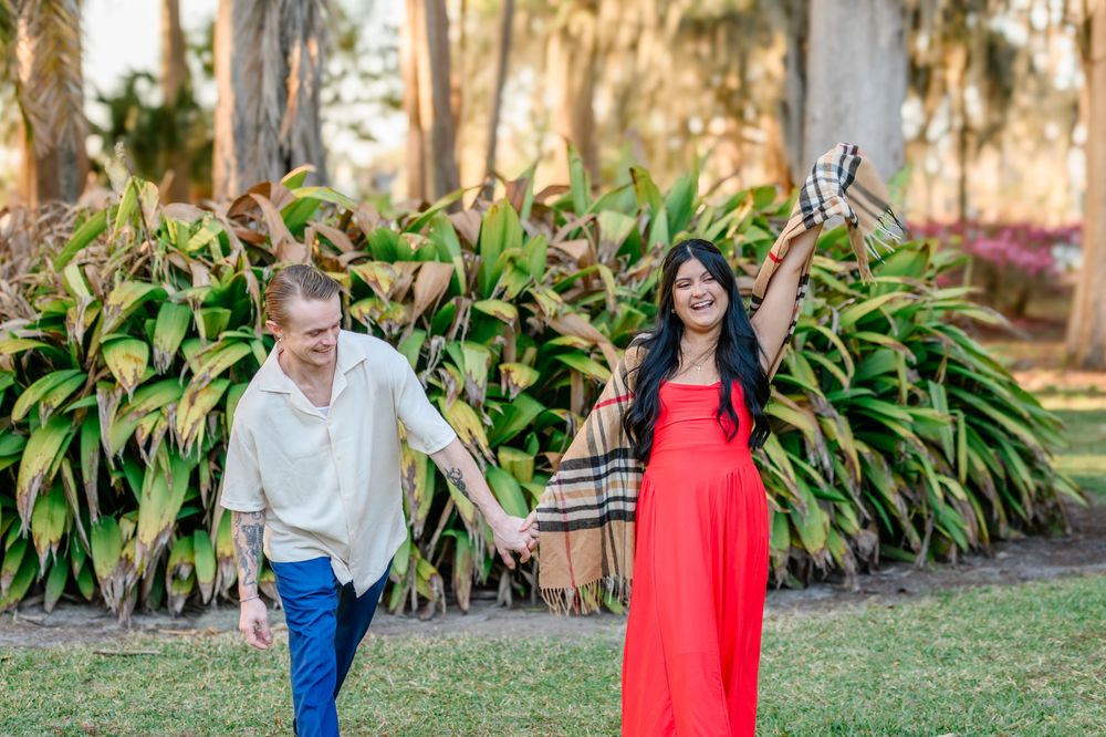 A couple holds hands while walking through a garden with tropical plants and trees.