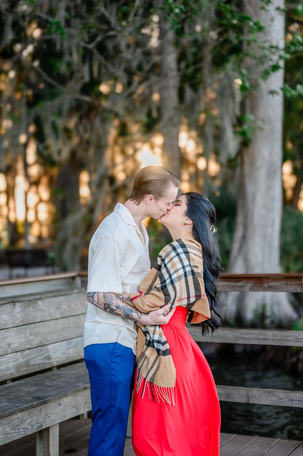 A romantic moment captured on a wooden bench surrounded by mossy trees at sunset.