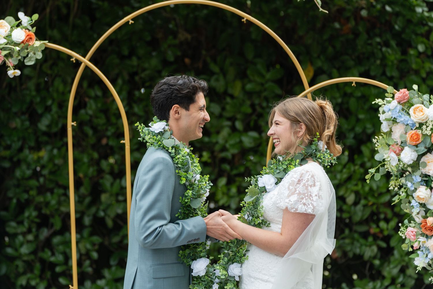 A couple shares a romantic moment under an elegant floral arch decorated with white blooms at an outdoor wedding ceremony.