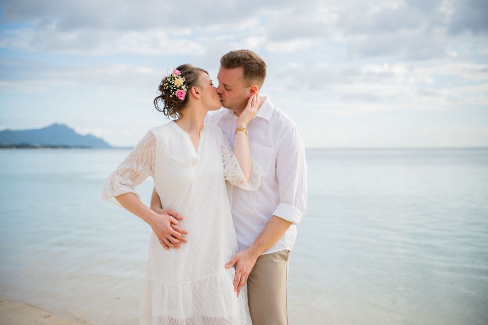 A romantic beach wedding scene with a couple embracing by the ocean with mountains in the background. Shot by Luminair Studio