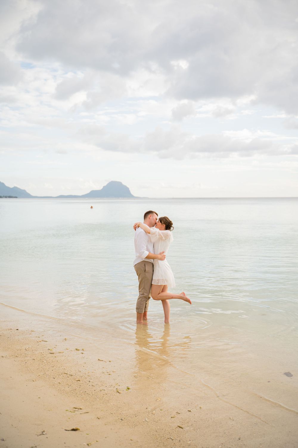 Romantic couple embracing on a scenic beach with cloudy skies and ocean views. Shot by Luminair Studio
