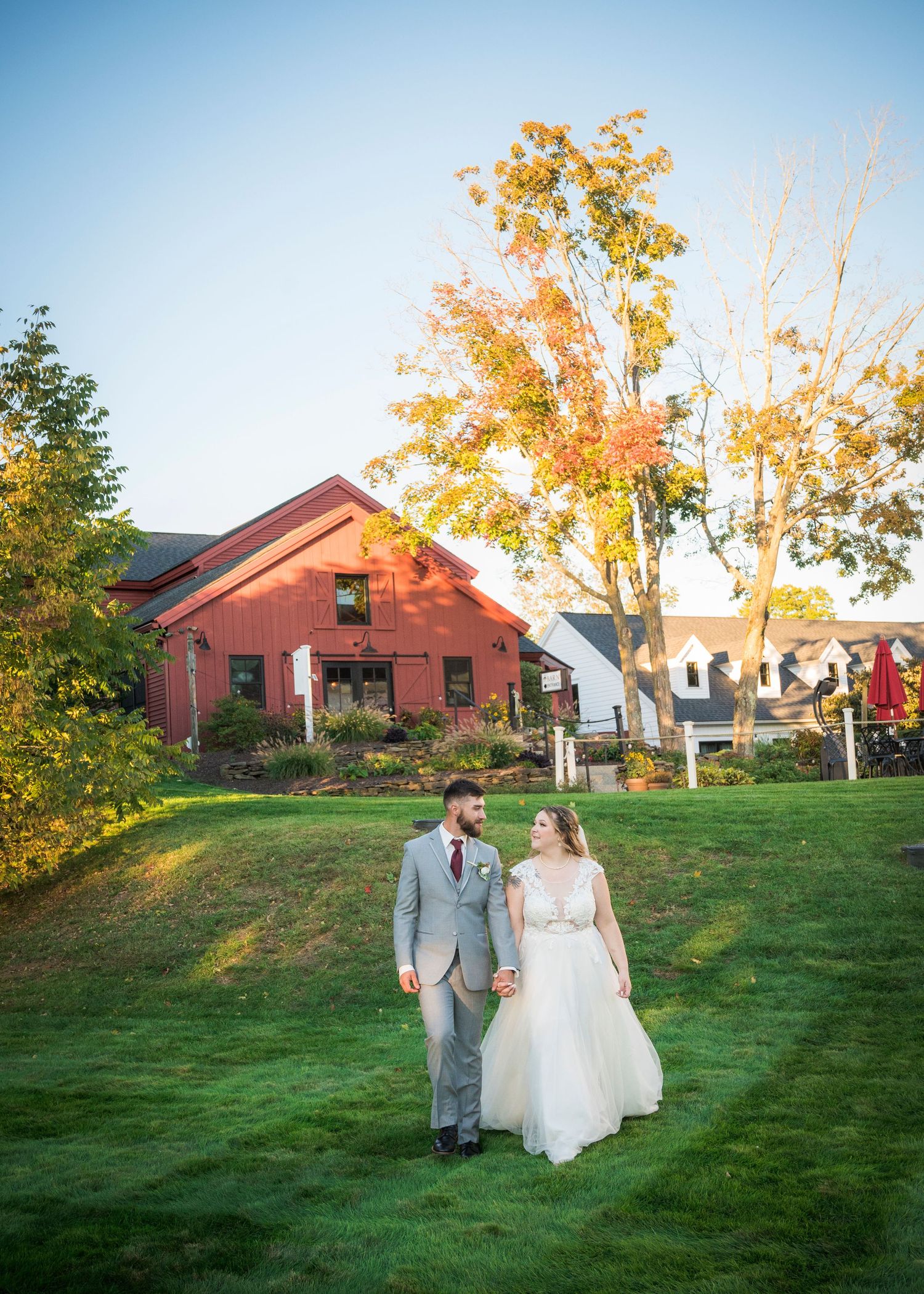 A couple walks together on a lush green hillside lawn at sunset with a brick building in the background.