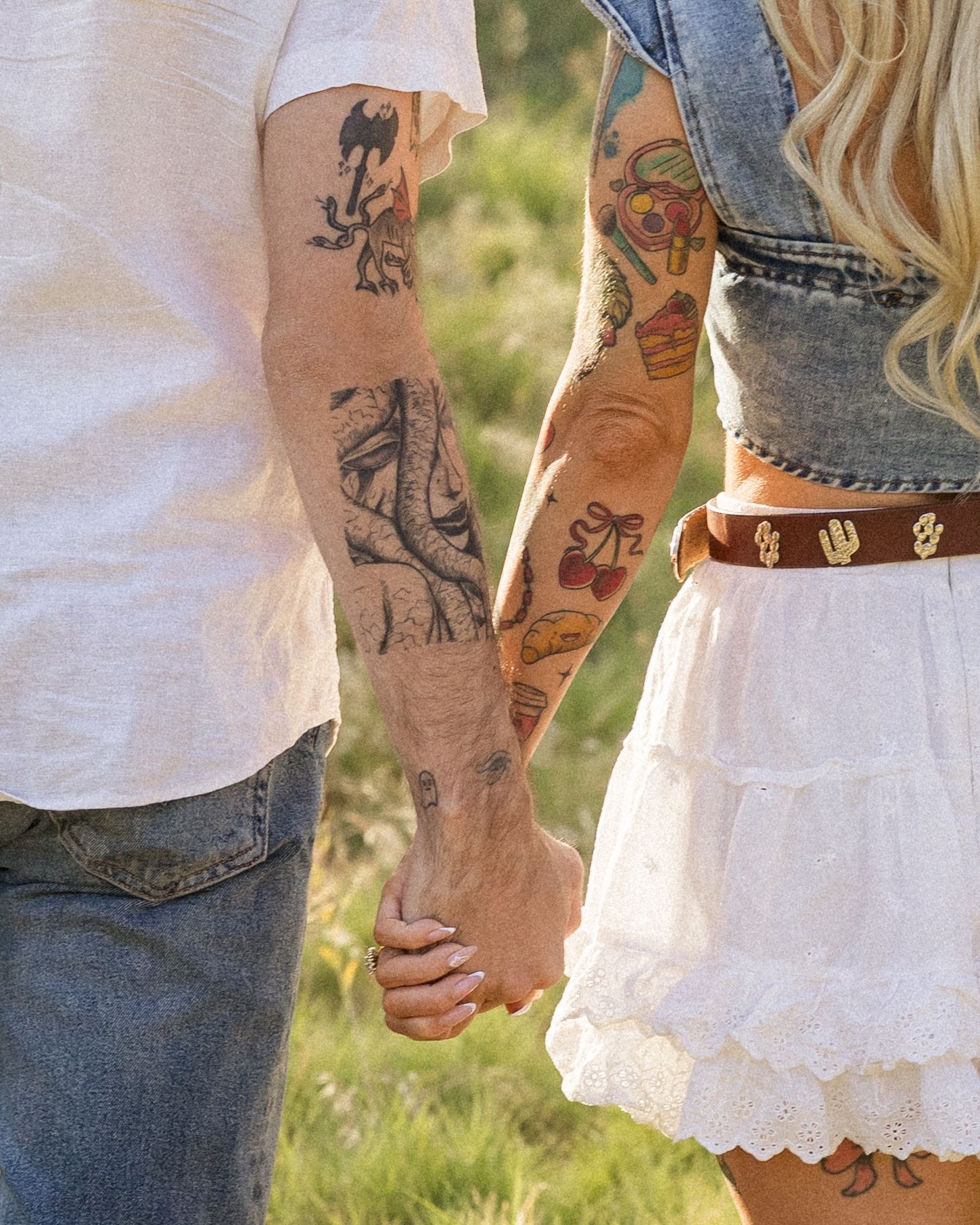 Close-up view of tattooed arms embracing in casual clothing against a sunlit outdoor background.